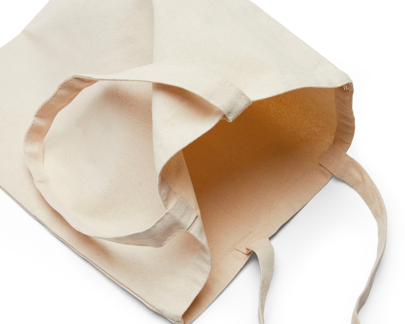 May include: A plain, off-white canvas tote bag with a single, long handle. The bag is empty and open, showing the inside of the bag.