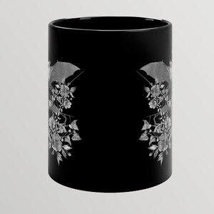May include: Black ceramic mug with a white design of bats and flowers. The design is mirrored on both sides of the mug.