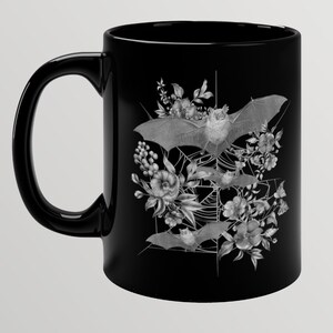 May include: Black ceramic mug with a white design of bats and flowers. The bats are flying in a web-like pattern with flowers surrounding them.