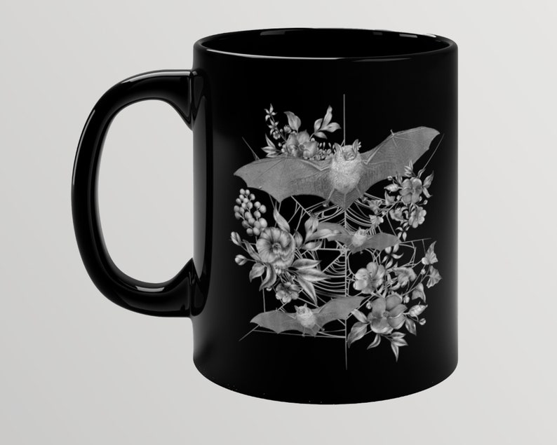 May include: Black ceramic mug with a white design of bats and flowers. The bats are flying in a web-like pattern with flowers surrounding them.