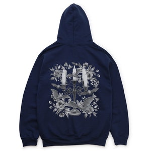 May include: A navy blue hooded sweatshirt featuring a graphic print of a candelabra with three lit candles, bats, and flowers. The graphic is in shades of grey.