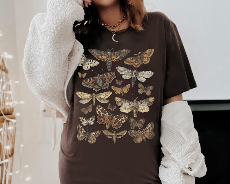 May include: A brown t-shirt with a print of various butterflies in shades of brown, yellow, and white. The butterflies are arranged in a random pattern on the shirt.