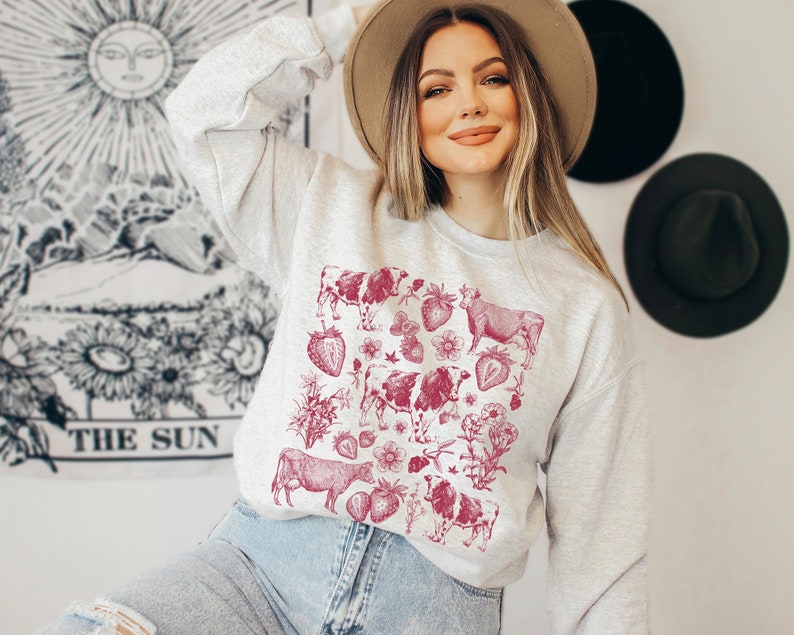 May include: A gray sweatshirt with a red vintage-style print of cows and strawberries. The print is centered on the front of the sweatshirt.