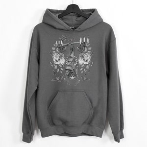May include: Gray hoodie with a detailed black and white illustration of a bat hanging upside down from a branch, surrounded by flowers and candles. The hoodie has a front pocket and a hood.