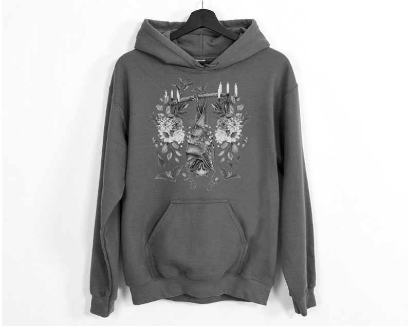 May include: Gray hoodie with a detailed black and white illustration of a bat hanging upside down from a branch, surrounded by flowers and candles. The hoodie has a front pocket and a hood.