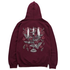 May include: Burgundy hooded sweatshirt with a graphic print of a candelabra with bats and roses. The candelabra has three candles and is surrounded by bats and roses.