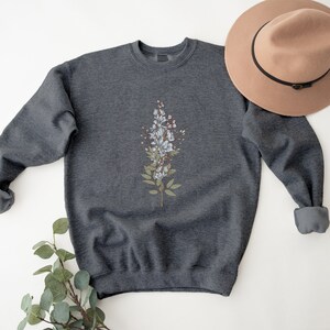 May include: A dark gray sweatshirt with a white floral design on the front. The sweatshirt has a crew neck and long sleeves.