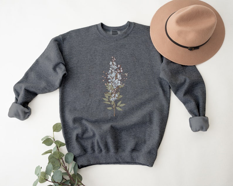 May include: A dark gray sweatshirt with a white floral design on the front. The sweatshirt has a crew neck and long sleeves.