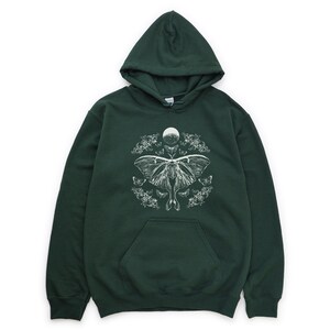 May include: A dark green hooded sweatshirt featuring a white print of a moth and moon design. The moth is surrounded by smaller moths and floral elements.
