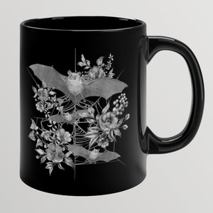 May include: Black ceramic mug with a white design of bats flying through a spiderweb with flowers.