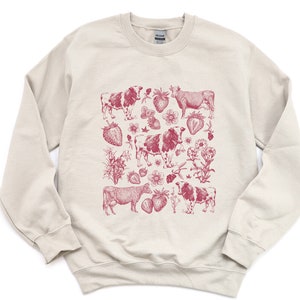 May include: A cream-colored sweatshirt with a red graphic print of cows and strawberries. The print is a vintage-style illustration.