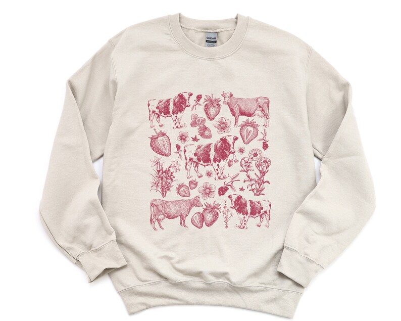 May include: A cream-colored sweatshirt with a red graphic print of cows and strawberries. The print is a vintage-style illustration.