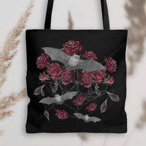 May include: Black tote bag with a design of bats and red roses on a black background. The bats are flying over the roses and there is a spiderweb in the background.