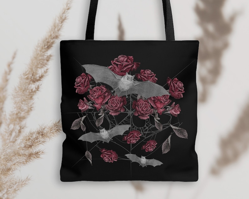 May include: Black tote bag with a design of bats and red roses on a black background. The bats are flying over the roses and there is a spiderweb in the background.