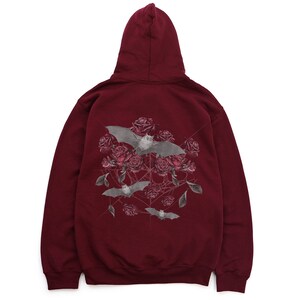 May include: Burgundy hoodie with a hood. The back features a graphic of gray bats, red roses, and a spiderweb design. The bats are in flight, and the roses are in full bloom. The hoodie is made of a soft material.