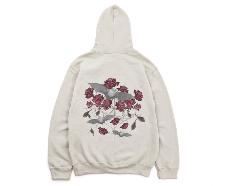 May include: A beige hoodie featuring a graphic design on the back. The design includes gray bats, dark red roses, and a spiderweb-like pattern. The hoodie has a hood and a relaxed fit, suitable for casual wear.