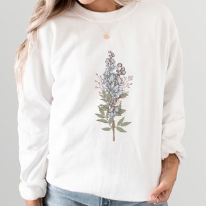 May include: White sweatshirt with a floral design featuring blue flowers and green leaves.