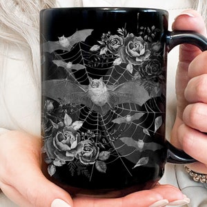 Pu&ograve; includere: Tazza da caff&egrave; nera con un design bianco e grigio di pipistrelli, rose e una ragnatela.