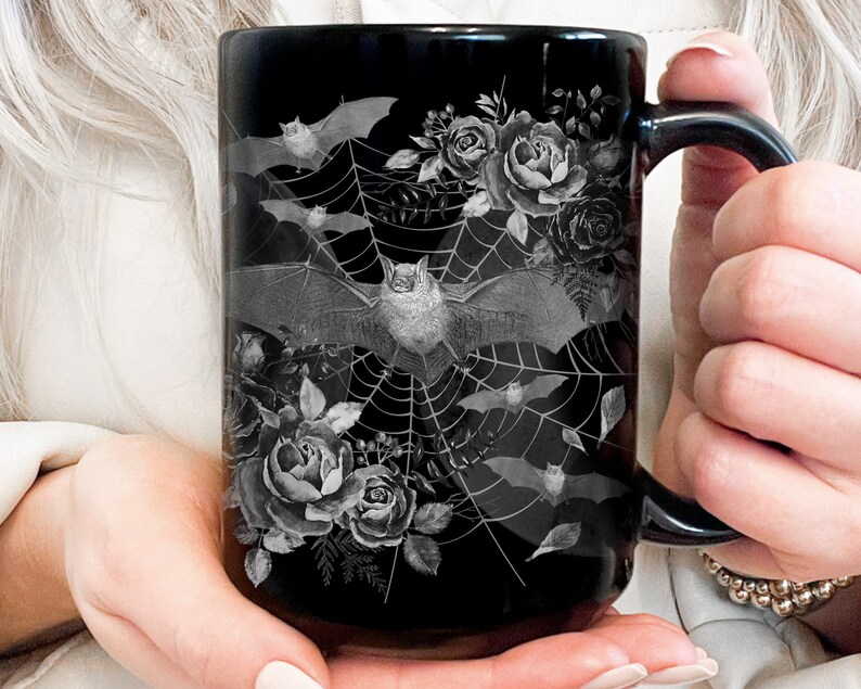 Pu&ograve; includere: Tazza da caff&egrave; nera con un design bianco e grigio di pipistrelli, rose e una ragnatela.