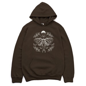 May include: A brown hooded sweatshirt featuring a white graphic print of a moth and moon surrounded by floral designs.