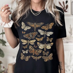 May include: Black t-shirt with a vintage illustration of various butterflies and moths in shades of brown, white, and black.