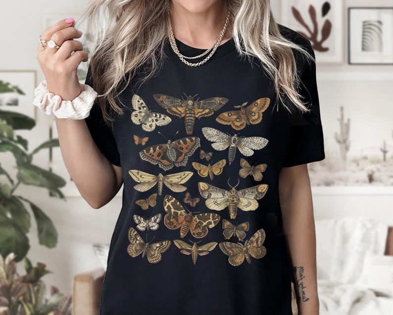 May include: Black t-shirt with a vintage illustration of various butterflies and moths in shades of brown, white, and black.