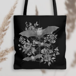 May include: Black tote bag with a white design of bats and flowers. The bats are flying in a web-like pattern with flowers and leaves around them.