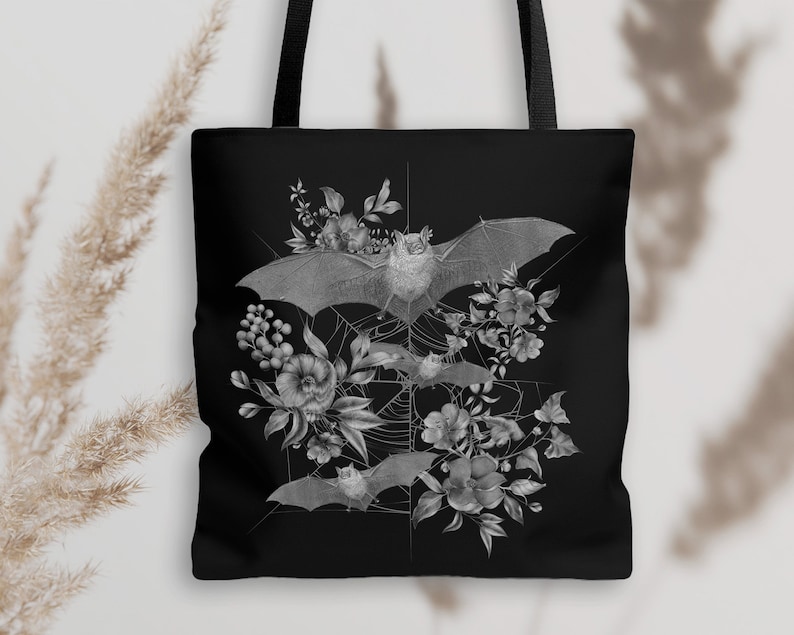 May include: Black tote bag with a white design of bats and flowers. The bats are flying in a web-like pattern with flowers and leaves around them.