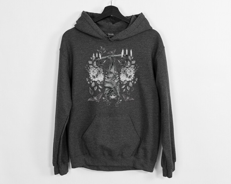 May include: Dark gray hoodie with a floral and bat design. The graphic features a bat hanging upside down from a branch, surrounded by flowers and candles. The hoodie has a front pocket and a hood.