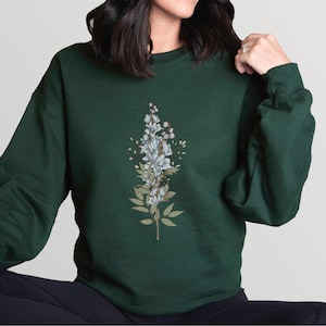 May include: A dark green sweatshirt with a floral design featuring white flowers and green leaves.