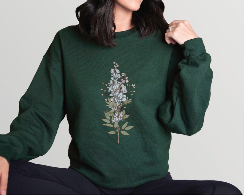 May include: A dark green sweatshirt with a floral design featuring white flowers and green leaves.