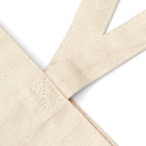 May include: Close-up of the top of a natural canvas tote bag with two straps meeting at the top. The straps are sewn together with a reinforced stitch.