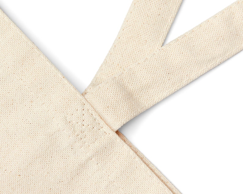 May include: Close-up of the top of a natural canvas tote bag with two straps meeting at the top. The straps are sewn together with a reinforced stitch.