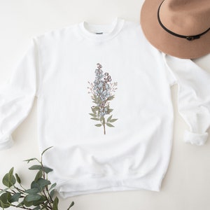 May include: White sweatshirt with a floral design featuring blue and brown flowers and green leaves.