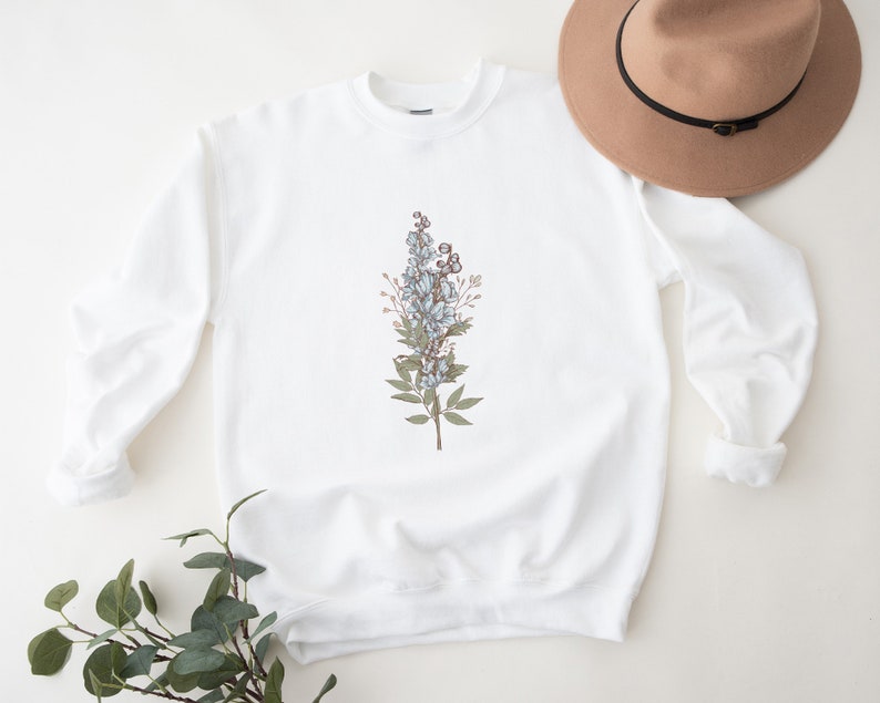 May include: White sweatshirt with a floral design featuring blue and brown flowers and green leaves.