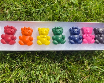 May include: A set of eight small bear-shaped crayons in a white box. The crayons are red, orange, yellow, green, blue, pink, purple, and black.