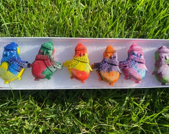 May include: Six small penguin-shaped ornaments with glitter and colorful paint. Each penguin has a different color scheme, including red, yellow, green, blue, purple, and pink.