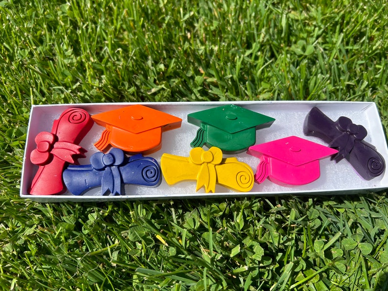 K&ouml;nnte beinhalten: Ein Set mit sechs Abiball-Kreiden in einer wei&szlig;en Schachtel. Die Kreiden sind in Form von Abschlusskappen und -zeugnissen. Die Farben sind rot, orange, gelb, gr&uuml;n, lila und rosa.
