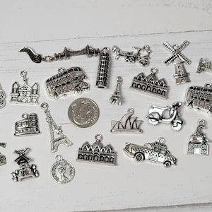 May include: A collection of silver charm pendants featuring various landmarks and transportation from around the world, including a double-decker bus, a scooter, the Eiffel Tower, and the Sydney Opera House.
