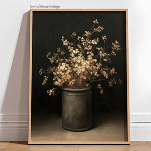 May include: A framed art print featuring a still life of dried flowers in a dark gray pot against a black background. The flowers are a light beige color, and the pot is cylindrical. The frame is a light brown color.