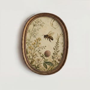 Op de afbeelding: Een ovaalvormig wandkunstwerk met een gedetailleerde illustratie van een honingbij die tussen diverse wilde bloemen en bladeren vliegt. Het kunstwerk is gevat in een getextureerde, antiek ogende bronzen lijst met een licht, crèmekleurige achtergrond.