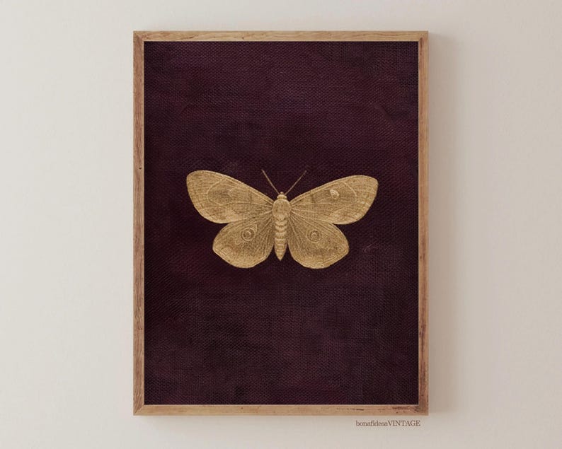 May include: A framed print featuring a gold-colored butterfly against a deep purple background. The butterfly is centered, with detailed wing patterns. The frame is a light brown color. The print has a vintage aesthetic.