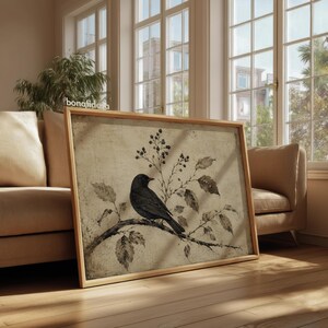 Peut inclure: Une &oelig;uvre d'art murale rectangulaire encadr&eacute;e repr&eacute;sentant un oiseau noir perch&eacute; sur une branche avec des feuilles et des baies. L'illustration pr&eacute;sente un fond textur&eacute; neutre et est ins&eacute;r&eacute;e dans un cadre en bois clair, avec le texte bonafide.