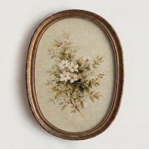 May include: Oval framed floral print. The artwork features a bouquet of white flowers and green leaves against a beige background. The frame is a detailed gold color, adding a vintage aesthetic.