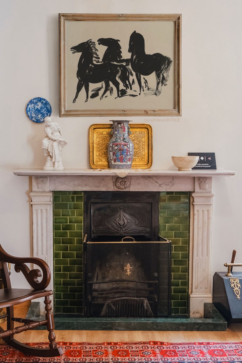 May include: A white marble fireplace with a green tiled surround and a black metal fireplace screen. A vase with a colorful floral design sits on the mantel above the fireplace, along with a framed black and white print of horses.