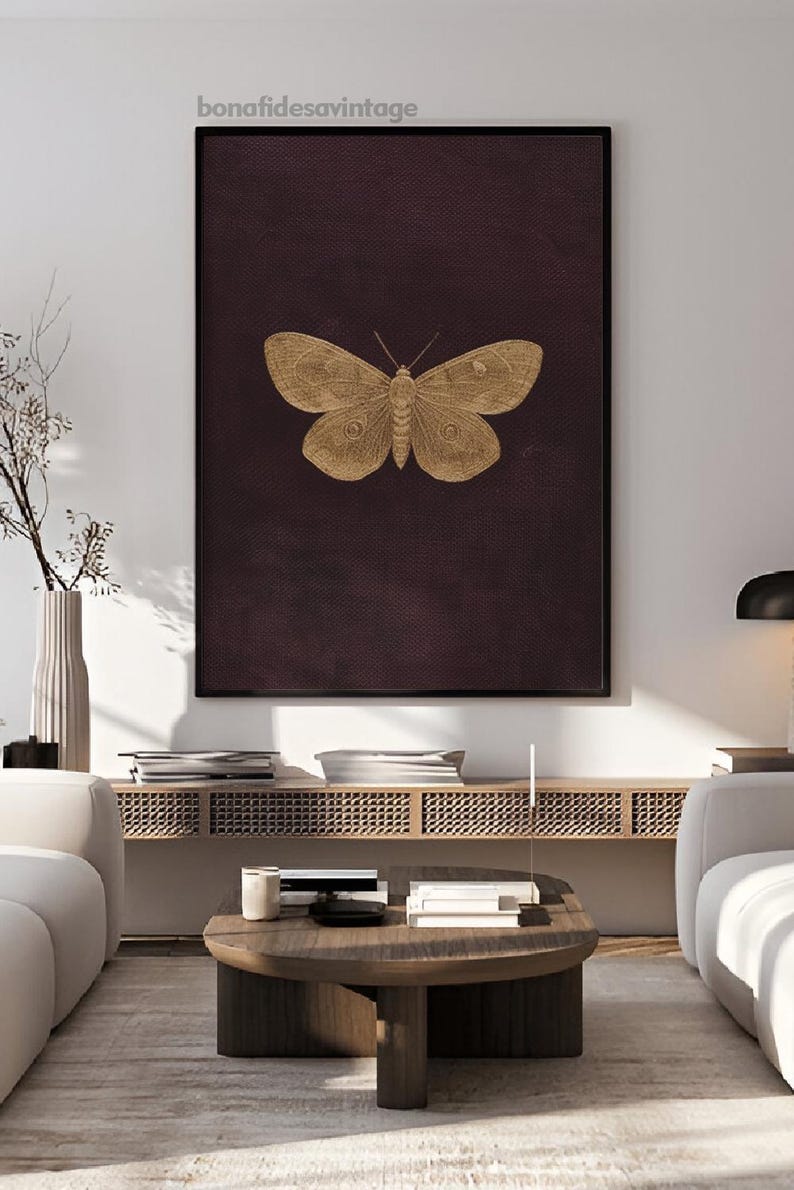 May include: A framed wall art print featuring a gold-colored butterfly illustration on a dark burgundy background. The artwork is displayed in a modern living room setting, with the text "bonafidesavintage" in the top left corner.
