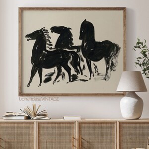 May include: A framed black and white illustration of three horses in a minimalist style. The horses are drawn in a simple, abstract style with bold lines. The background is a light beige color.