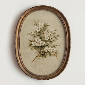 May include: Oval framed floral print featuring a branch of white blossoms and green leaves. The artwork is set against a beige background and framed in a gold-toned, ornate oval frame. A vintage-style botanical print.