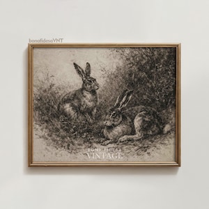 Puede incluir: Una impresión vintage enmarcada que presenta dos conejos en un entorno natural. La obra de arte es en blanco y negro, con sombreado y textura detallados. El marco es de color dorado cálido, con el texto "bonafidesaVNT" y "VINTAGE".