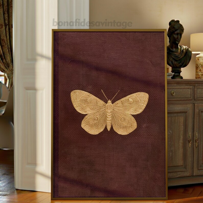 May include: A framed artwork featuring a detailed gold butterfly illustration on a deep burgundy background. The artwork has a gold frame and the text "bonafidesavintage" at the top. The butterfly is centered, showcasing its intricate wing patterns.